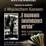 Wojciech Kass siedzący przy stole z mikrofonem podczas spotkania autorskiego
