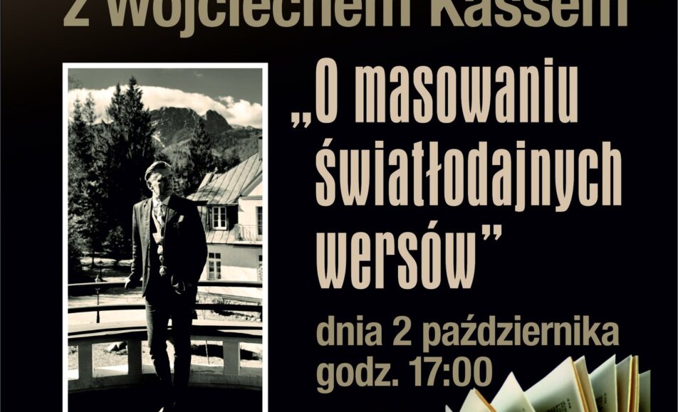 Wojciech Kass siedzący przy stole z mikrofonem podczas spotkania autorskiego